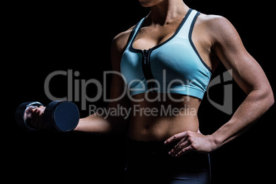 Midsection of woman lifting dumbbell