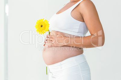 Pregnant woman touching her belly while holding yellow flower