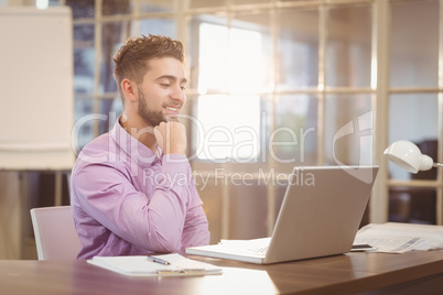 Businessman with hand on chin working with laptop