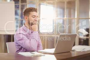 Businessman with hand on chin working with laptop