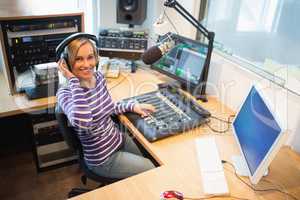 Happy female radio host at sound mixer desk in studio