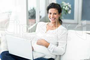 Portrait of happy woman using laptop on sofa