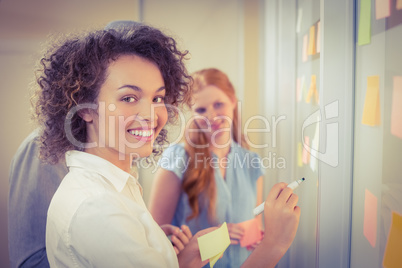 Portrait businesswoman writing on glass as colleagues looking at