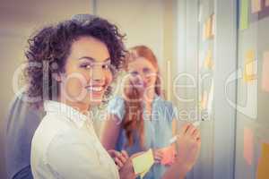 Portrait businesswoman writing on glass as colleagues looking at