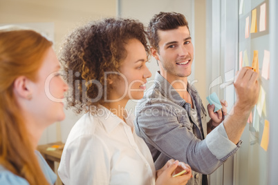 Businessman writing on glass as female colleagues looking at it