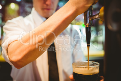 Barkeeper holding beer glass below dispenser tap