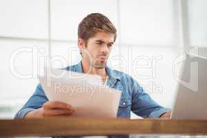 Hipster holding documents while working on laptop in office
