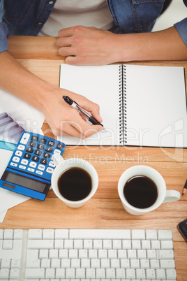 Hipster writing on spiral notebook at desk in office