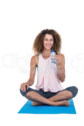 Young woman with water bottle sitting on exercise mat