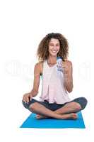 Young woman with water bottle sitting on exercise mat