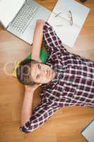 Hipster with hands behind head lying on hardwood floor
