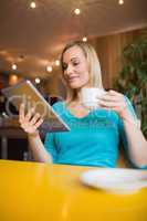 Young woman using digital tablet while holding coffee cup