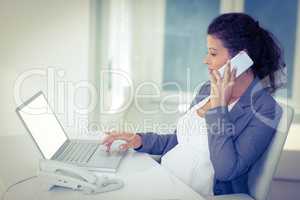 Pregnant businesswoman talking on mobile phone while working