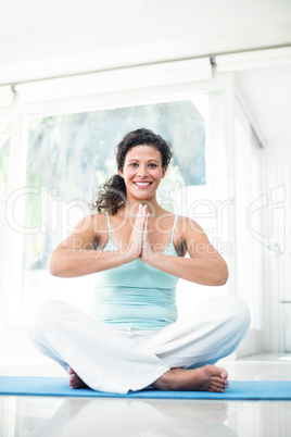 Pregnant woman sitting on exercise mat with joined hands