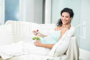 Portrait of happy woman with salad on sofa