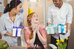Happy colleagues with gifts looking at businesswoman