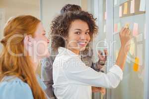 Portrait businesswoman writing on glass as colleagues looking at