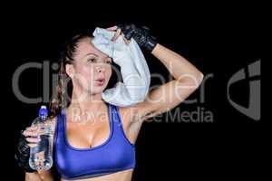 Tired woman wiping sweat while holding water bottle