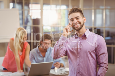 Businessman talking on phone in office with colleagues working