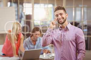 Businessman talking on phone in office with colleagues working