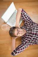 Creative businessman smiling while lying by laptop on hardwood f