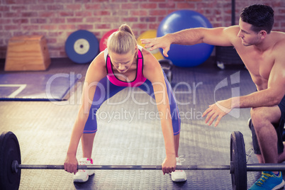 Woman lifting barbell with her trainer