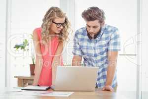 Man using laptop while discussing with woman at desk