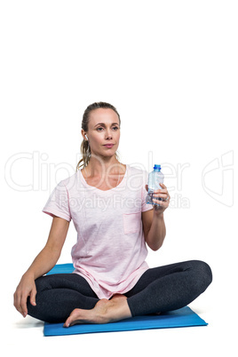 Thoughtful sporty woman with bottle resting on mat