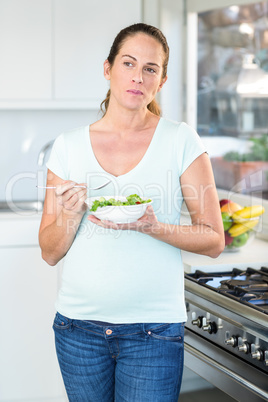 Happy woman eating fresh salad in kitchen