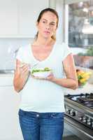 Happy woman eating fresh salad in kitchen
