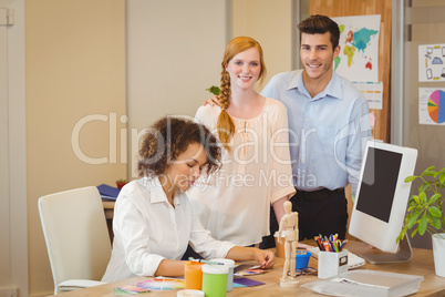 Business people standing by colleague working at desk