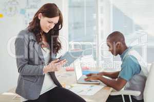 Woman using digital tablet while sitting on desk with man workin