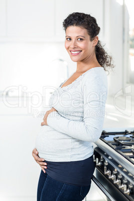 Pregnant woman touching her bellly while standing in kitchen