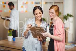 Happy businesswomen looking at clipboard in office