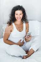 Happy beautiful woman using mobile phone while sitting on bed