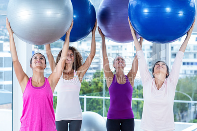 Cheerful women holding exercise balls with arms raised
