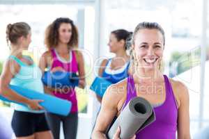 Portrait of cheerful woman holding exercise mat and smiling