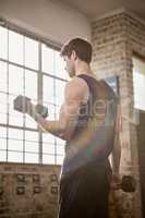 Rear view of focused man lifting dumbbells