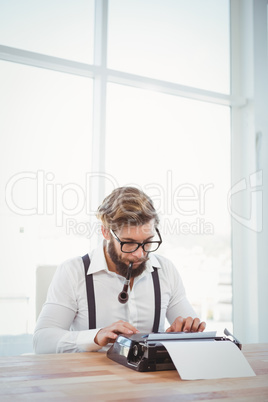 Hipster smoking pipe while working on typewriter
