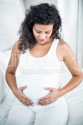 Woman touching her tummy while sitting on bed