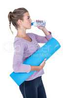 Woman drinking water while holding exercise mat
