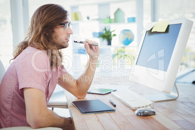 Hipster smoking electronic cigarette at computer desk in office