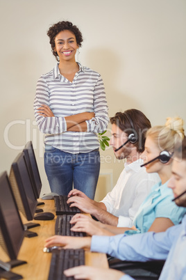 Smiling businesswoman with arms crossed standing at employees