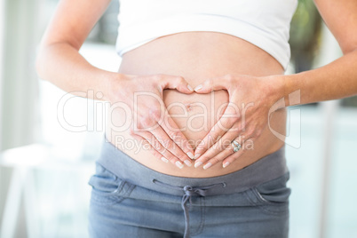 Midsection of woman hands making heart shape on belly