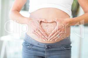 Midsection of woman hands making heart shape on belly