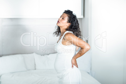 Pregnant woman holding her back while standing by bed