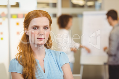 Serious businesswoman with arm crossed with colleagues in backgr