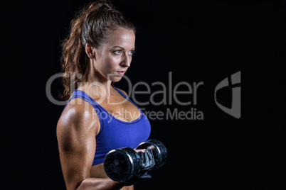 Side view of fit woman lifting dumbbell