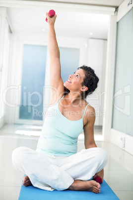 Pregnant woman lifting weight while sitting on exercise mat