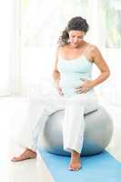 Pregnant woman touching her belly while sitting on exercise ball